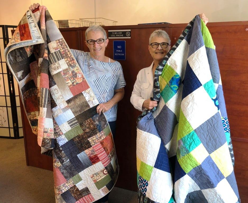 Two women hold up donated handmade quilts. 